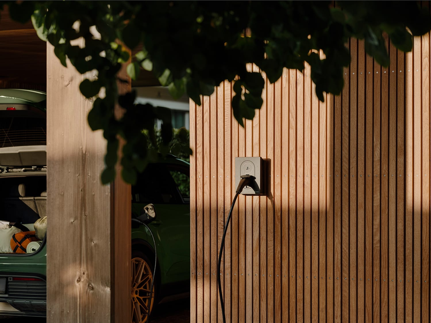 Zaptec Go laadstation op een houten gevel naast een elektrische wagen
